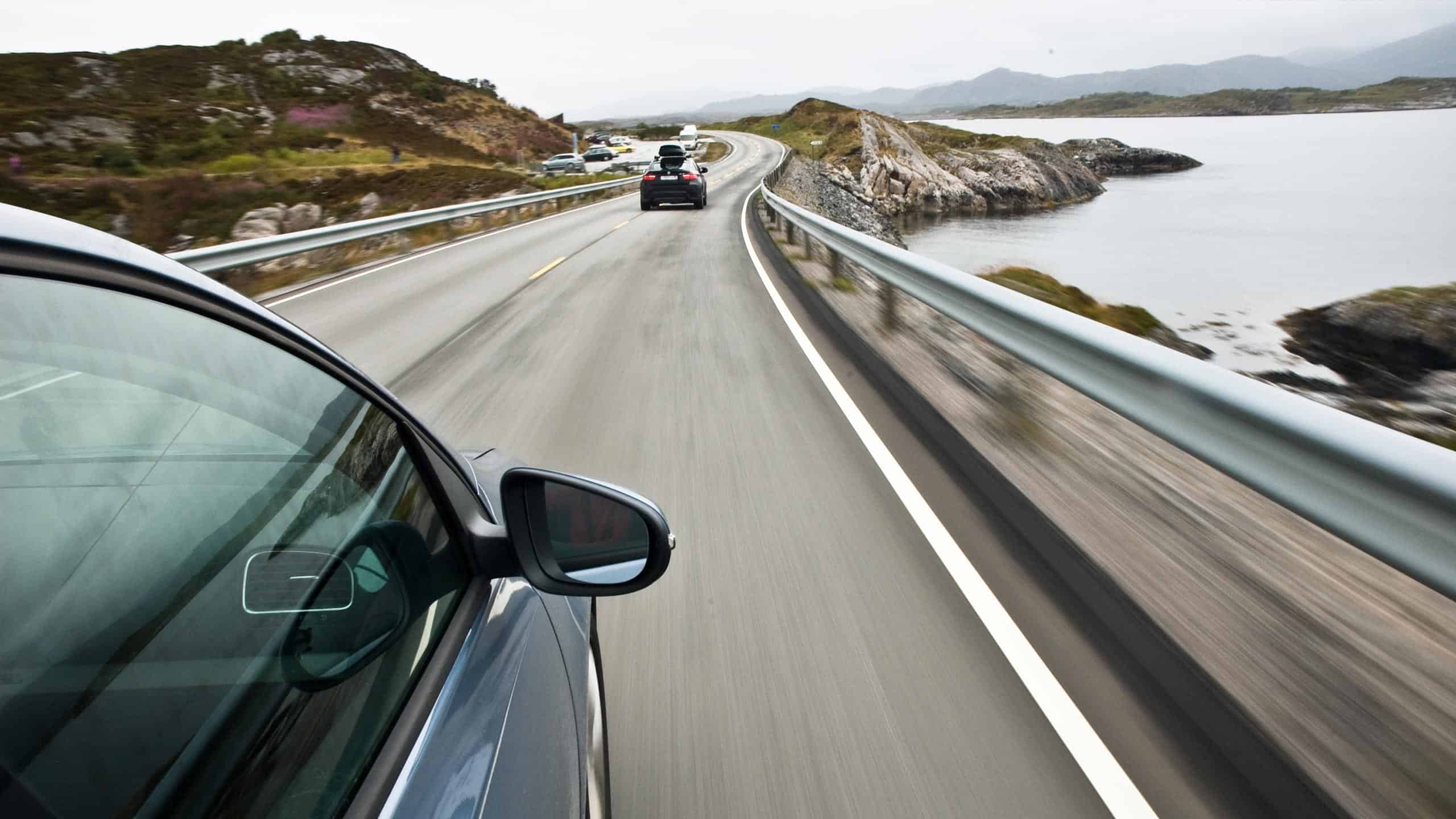 Førekortkandidat kjører bil langs naturskjønn vei ved sjøen, under trafikkopplæring, med fokus på sikker kjøring og trafikkopplæring i Norge.